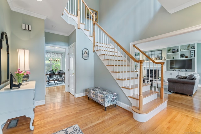 stairway featuring wood finished floors, crown molding, baseboards, a chandelier, and a high ceiling