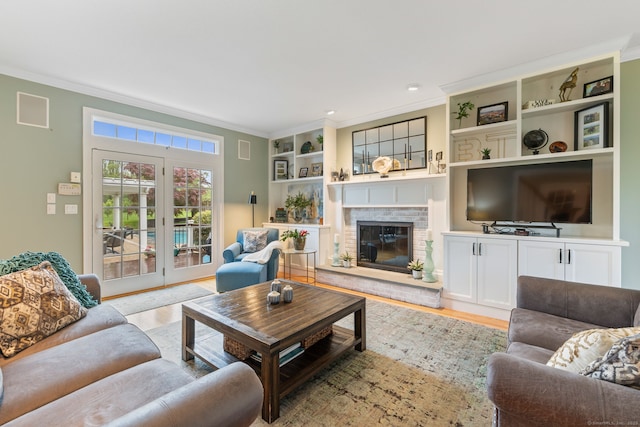 living area with ornamental molding, light wood-type flooring, built in features, and a fireplace