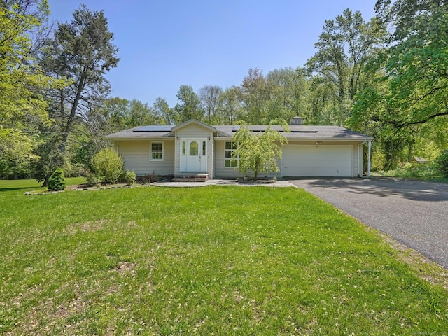 ranch-style home featuring a garage, driveway, a front lawn, roof mounted solar panels, and a chimney
