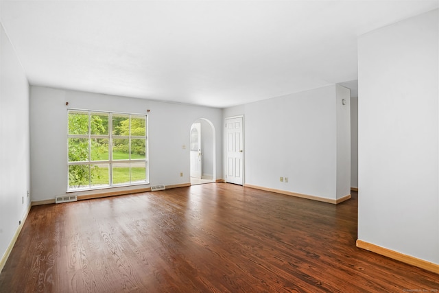 unfurnished living room with arched walkways, baseboards, and wood finished floors