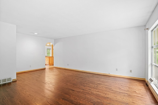 empty room featuring arched walkways, wood finished floors, healthy amount of natural light, baseboards, and recessed lighting