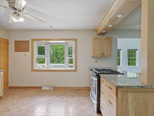 kitchen featuring gas stove, light brown cabinets, ceiling fan, light stone counters, and baseboards