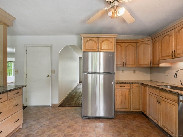 kitchen featuring freestanding refrigerator, a sink, ceiling fan, dark stone countertops, and dishwashing machine