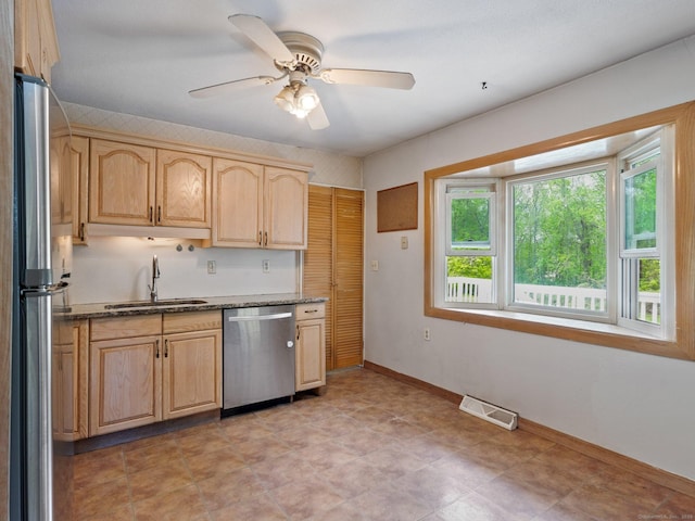 kitchen featuring a sink, appliances with stainless steel finishes, light brown cabinetry, and dark stone counters