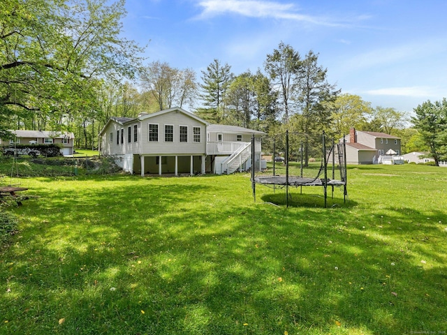 rear view of property with a trampoline, stairway, a yard, and a deck