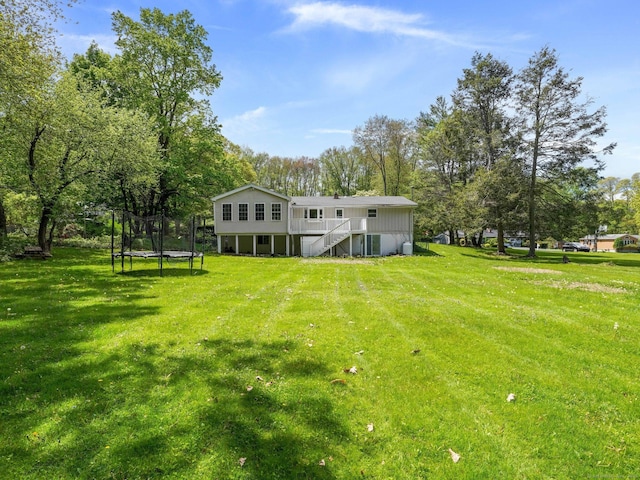 back of property with a trampoline, stairway, a lawn, a deck, and view of wooded area