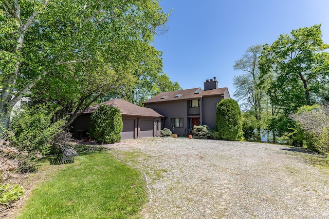 view of front of home featuring a garage, gravel driveway, a chimney, and stucco siding