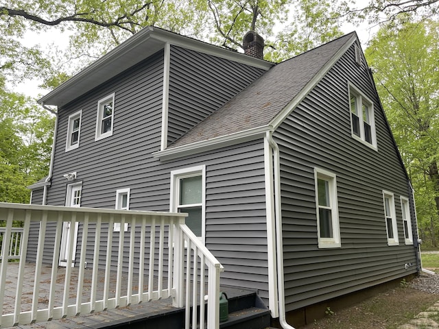 view of side of property featuring a chimney, a deck, and roof with shingles