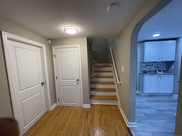 staircase with wood finished floors, arched walkways, baseboards, and recessed lighting