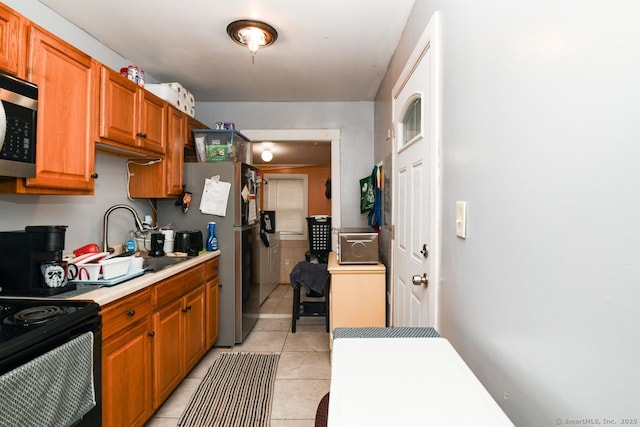 kitchen featuring stainless steel appliances, light tile patterned floors, light countertops, a sink, and brown cabinetry