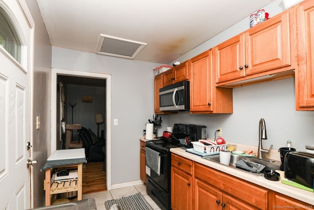 kitchen with stainless steel microwave, black range with electric stovetop, light countertops, light tile patterned floors, and brown cabinetry