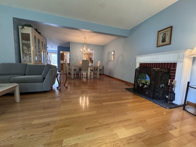 227 Twin Lakes Rd Apt C, North Branford, CT 06471 - living area featuring a chandelier, light wood-style flooring, a brick fireplace, baseboards, and a textured ceiling