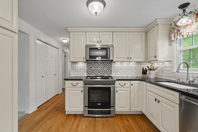 134 W Lake Ave, Guilford, CT 06437 - kitchen with appliances with stainless steel finishes, a sink, dark countertops, light wood-type flooring, and decorative backsplash