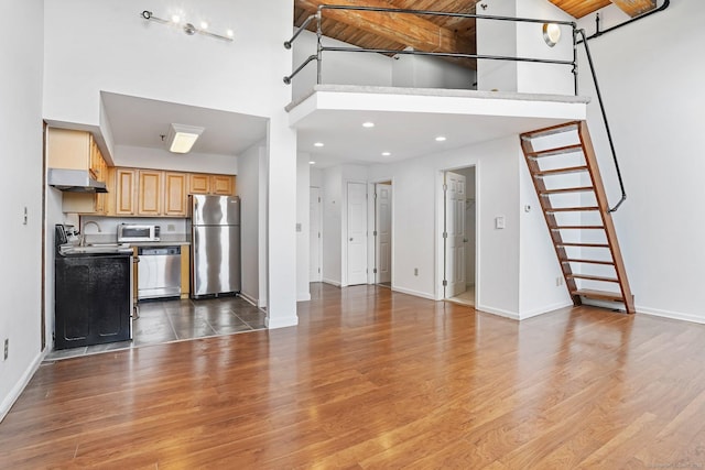25 Grand St Apt 102, Norwalk, CT 06851 - unfurnished living room featuring a towering ceiling, baseboards, wood finished floors, stairway, and recessed lighting
