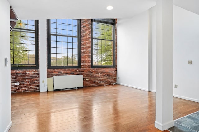 25 Grand St Apt 102, Norwalk, CT 06851 - unfurnished living room with radiator heating unit, brick wall, wood finished floors, and baseboards