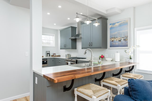276 Niantic River Rd, Waterford, CT 06385 - kitchen with butcher block countertops, wall chimney exhaust hood, a breakfast bar, a peninsula, and decorative light fixtures