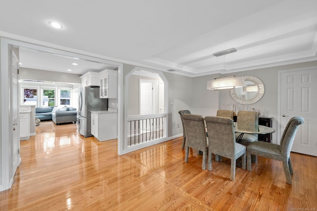 dining room featuring light wood-style floors, arched walkways, a tray ceiling, crown molding, and recessed lighting