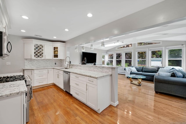 kitchen with open floor plan, stainless steel appliances, a peninsula, a sink, and white cabinets