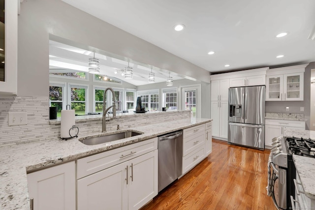 kitchen with stainless steel appliances, a sink, decorative backsplash, vaulted ceiling, and light wood finished floors