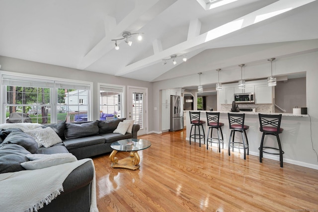 living room with vaulted ceiling, light wood-type flooring, baseboards, and a skylight