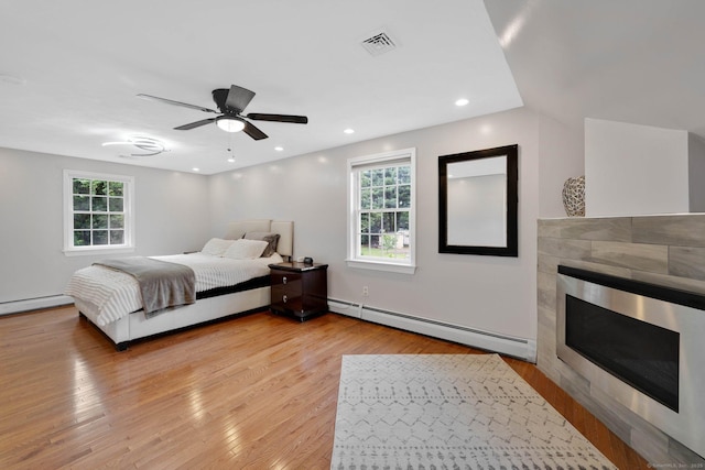 bedroom featuring baseboard heating, a tile fireplace, light wood finished floors, ceiling fan, and recessed lighting