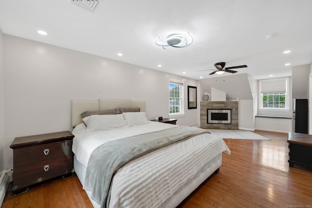 bedroom with baseboard heating, wood finished floors, baseboards, a fireplace, and recessed lighting