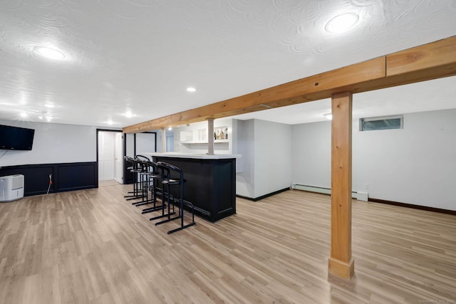 kitchen featuring open floor plan, a breakfast bar area, light countertops, light wood-type flooring, and baseboards