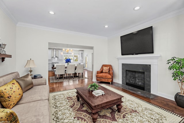 living area featuring wood finished floors, crown molding, a glass covered fireplace, a chandelier, and recessed lighting