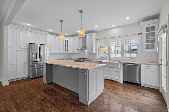 kitchen with appliances with stainless steel finishes, wall chimney range hood, a sink, white cabinetry, and recessed lighting