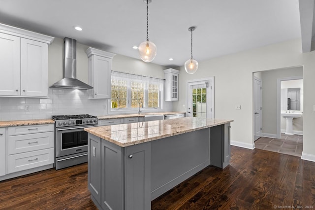 kitchen with stainless steel gas range, wall chimney range hood, a kitchen island, white cabinetry, and a sink