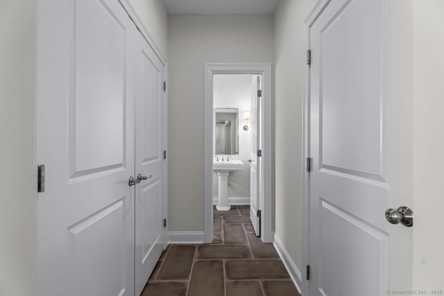 hall with baseboards, a sink, and dark tile patterned flooring