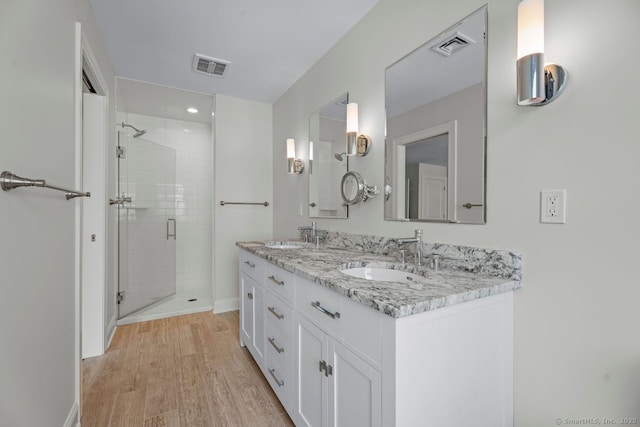 full bathroom featuring a stall shower, wood finished floors, double vanity, baseboards, and recessed lighting