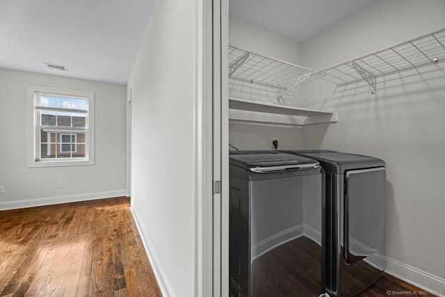 clothes washing area featuring washing machine and clothes dryer, wood finished floors, and baseboards
