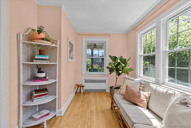 sitting room featuring radiator, light wood finished floors, crown molding, and baseboards