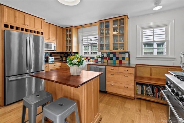 kitchen with appliances with stainless steel finishes, butcher block countertops, backsplash, and light wood-type flooring