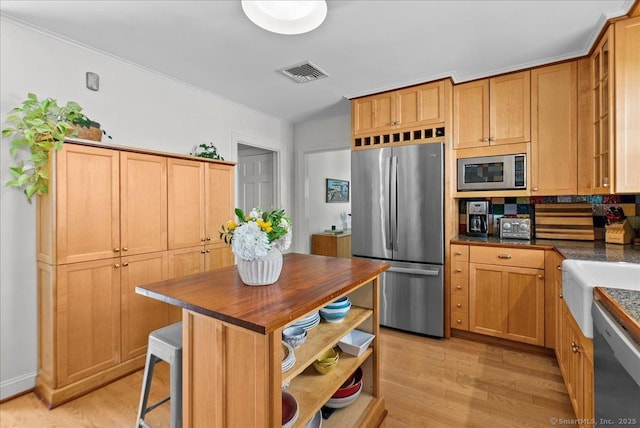 kitchen with stainless steel appliances, light wood-style flooring, ornamental molding, a kitchen bar, and wood counters