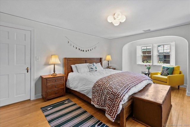 bedroom featuring light wood finished floors, arched walkways, and baseboards