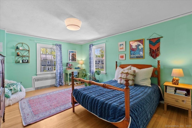 bedroom featuring radiator heating unit, wood finished floors, crown molding, a textured ceiling, and baseboards