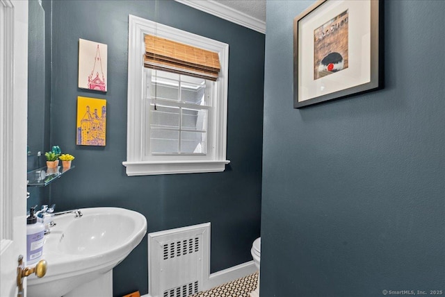 half bathroom with radiator heating unit, a sink, ornamental molding, baseboards, and toilet