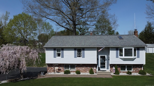 raised ranch featuring a chimney, a front yard, brick siding, and a shingled roof
