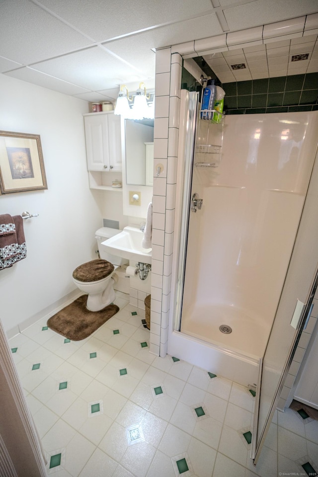 bathroom with a shower stall, a drop ceiling, a sink, tile patterned flooring, and toilet