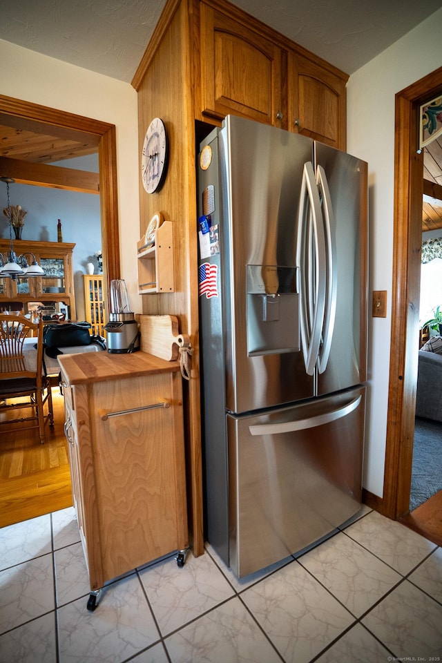kitchen with stainless steel refrigerator with ice dispenser, light marble finish floors, brown cabinetry, and butcher block countertops