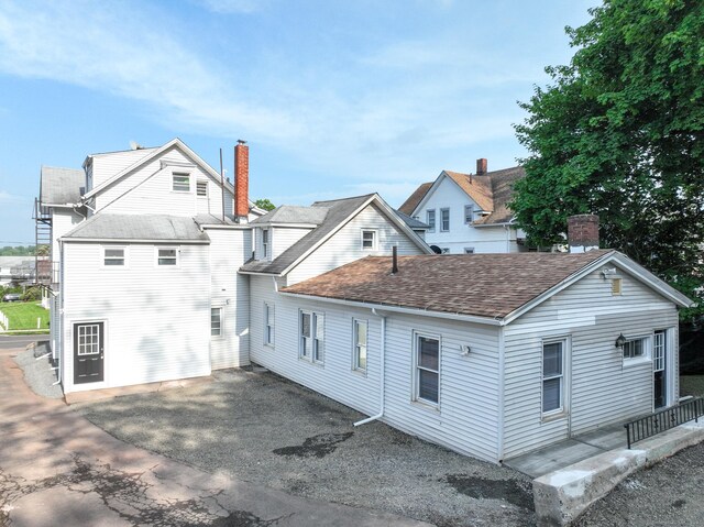 rear view of house featuring a patio area, a shingled roof, and a chimney