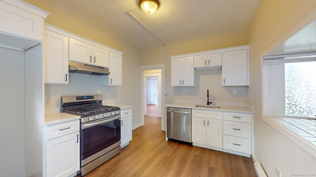 kitchen with appliances with stainless steel finishes, under cabinet range hood, a sink, white cabinets, and light countertops