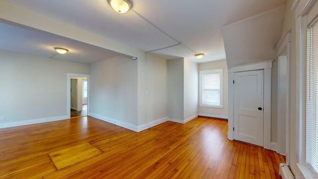 spare room featuring a baseboard radiator, light wood finished floors, plenty of natural light, and baseboards