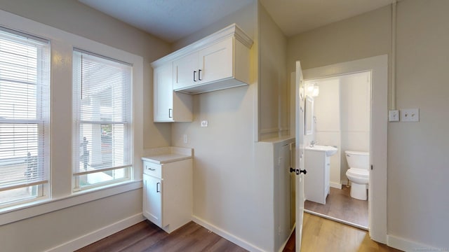 kitchen with wood finished floors, white cabinetry, light countertops, and baseboards