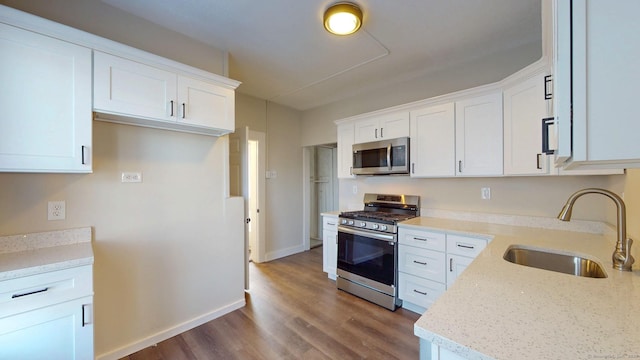kitchen with appliances with stainless steel finishes, a sink, wood finished floors, white cabinets, and light stone countertops