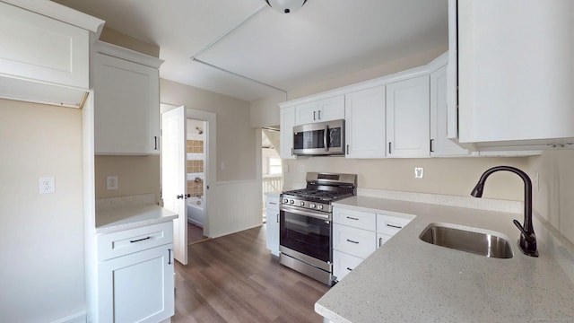 kitchen featuring stainless steel appliances, a sink, light stone counters, a wainscoted wall, and white cabinetry