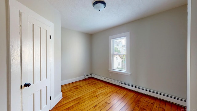 spare room featuring baseboard heating, light wood-style flooring, baseboards, and a textured ceiling