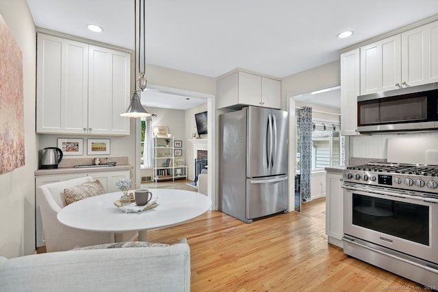 49 Bear Hills Rd, Newtown, CT 06470 - kitchen with stainless steel appliances, white cabinets, light wood-style floors, recessed lighting, and a glass covered fireplace